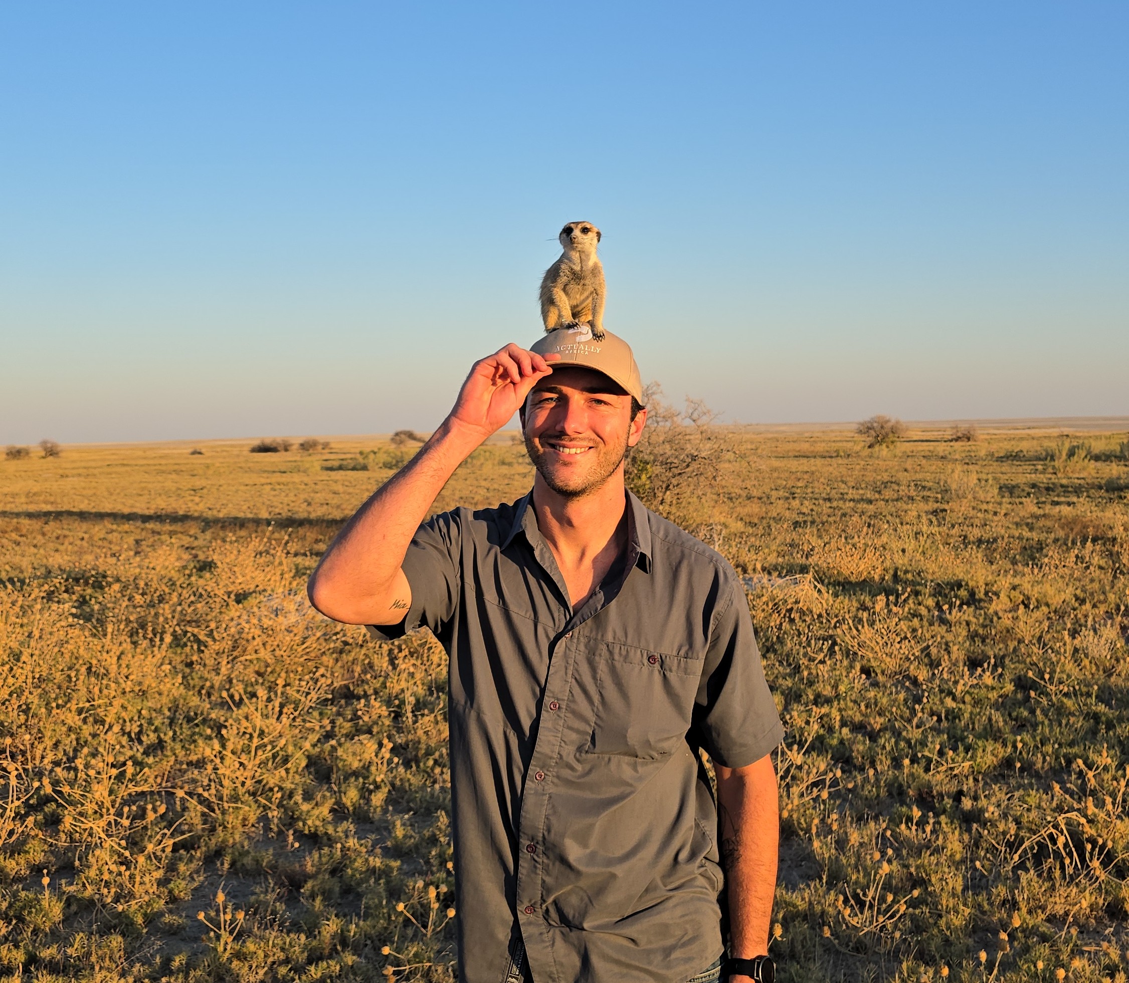 Jake in the Botswana landscape with a meerkat perched on his cap.