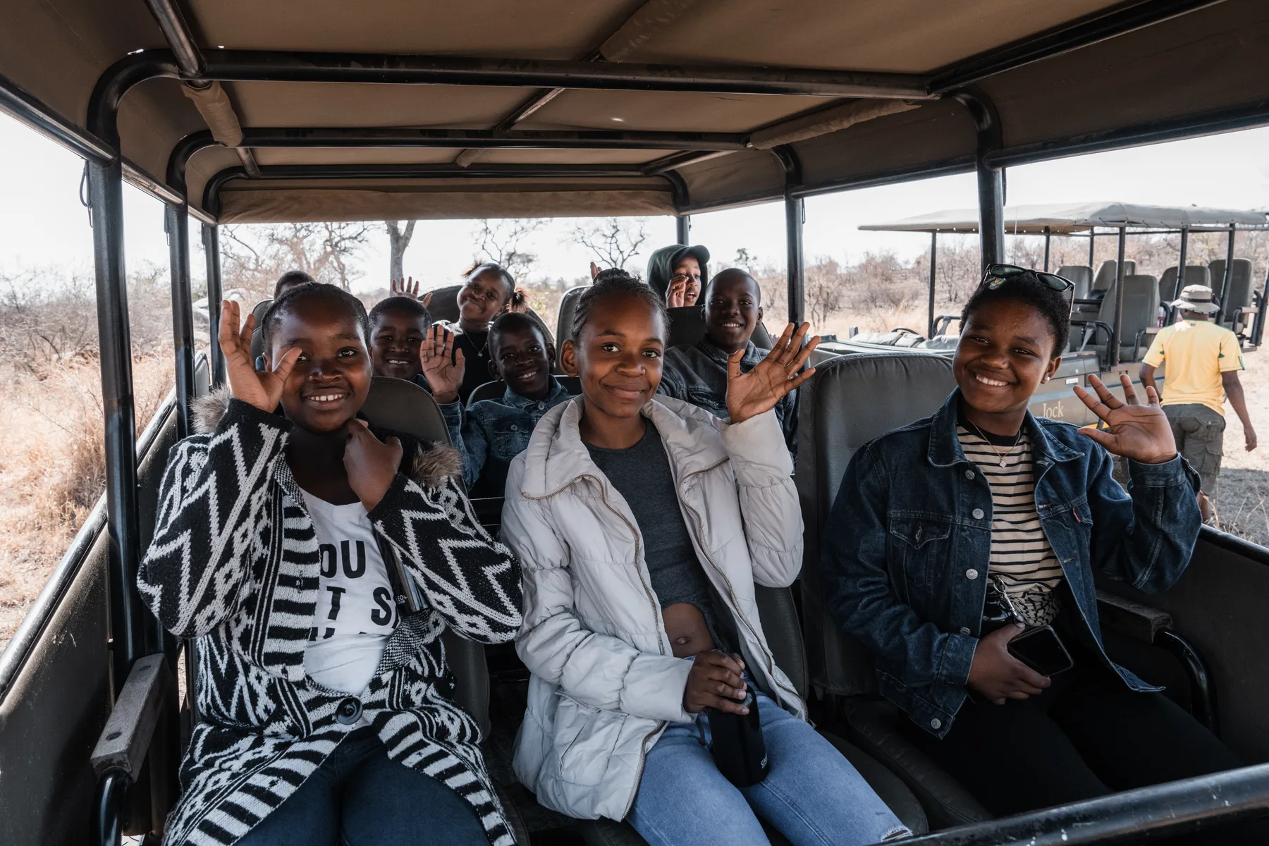Young people smiling and waving from a safari vehicle